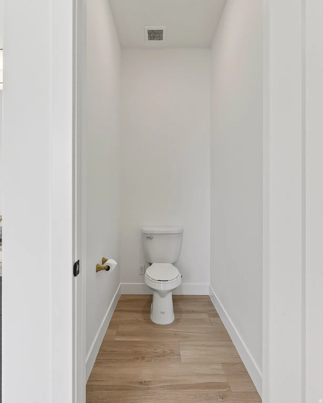 Compact powder room featuring wood-finish flooring, white baseboards, and a white toilet