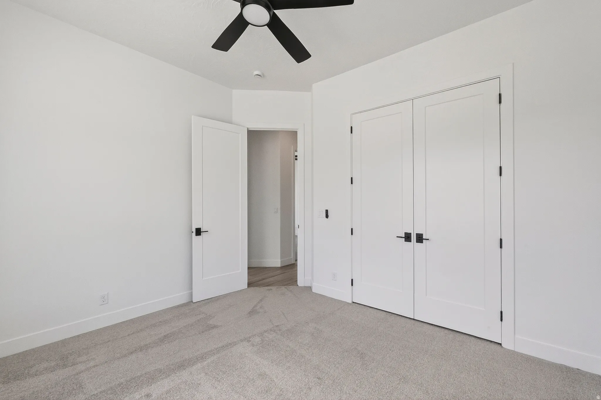 Room featuring light-toned carpeting, white walls, and a modern ceiling fan