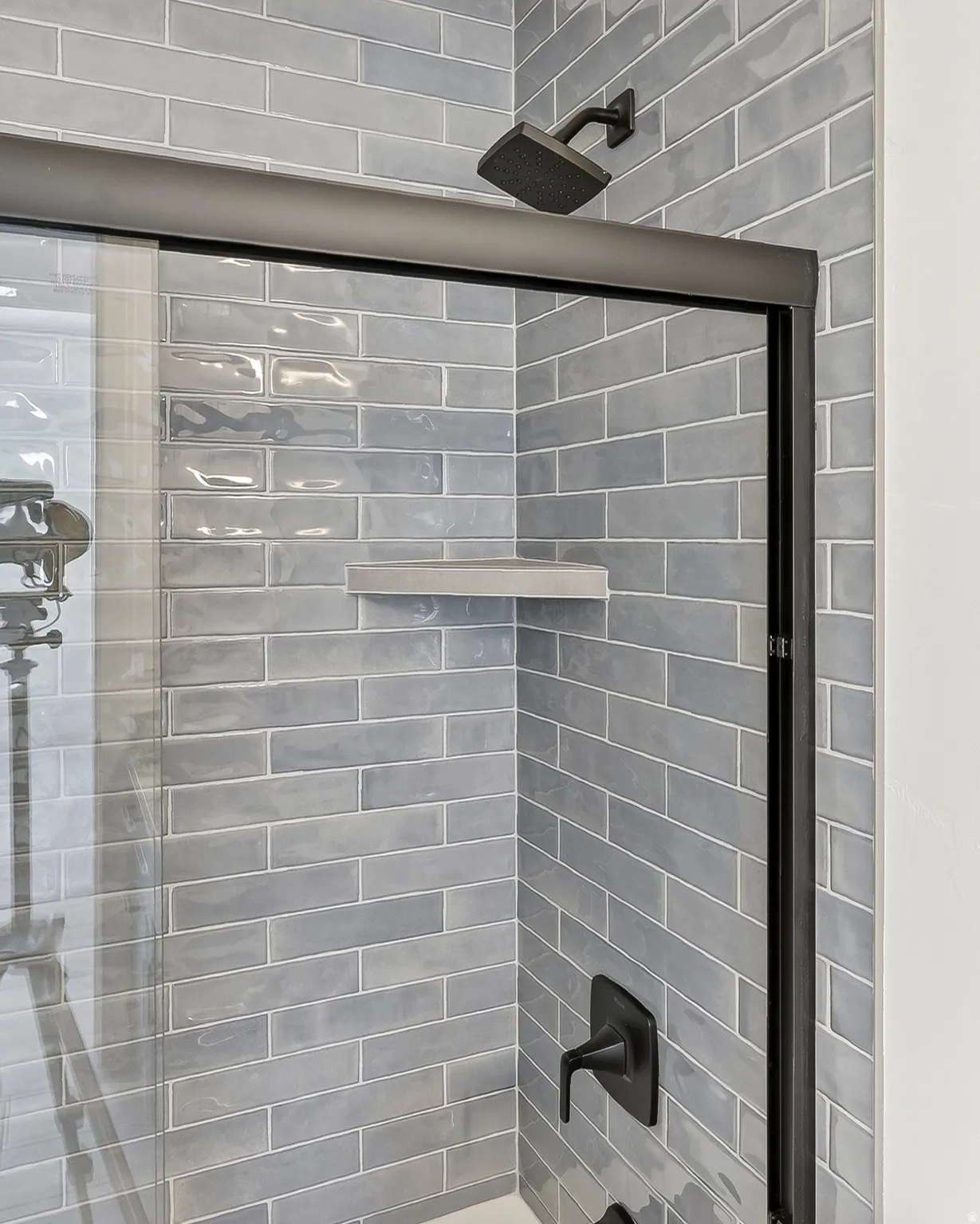 Shower enclosure featuring subway tile, a rain showerhead, matte black fixtures, a built-in corner shelf, and a framed glass door