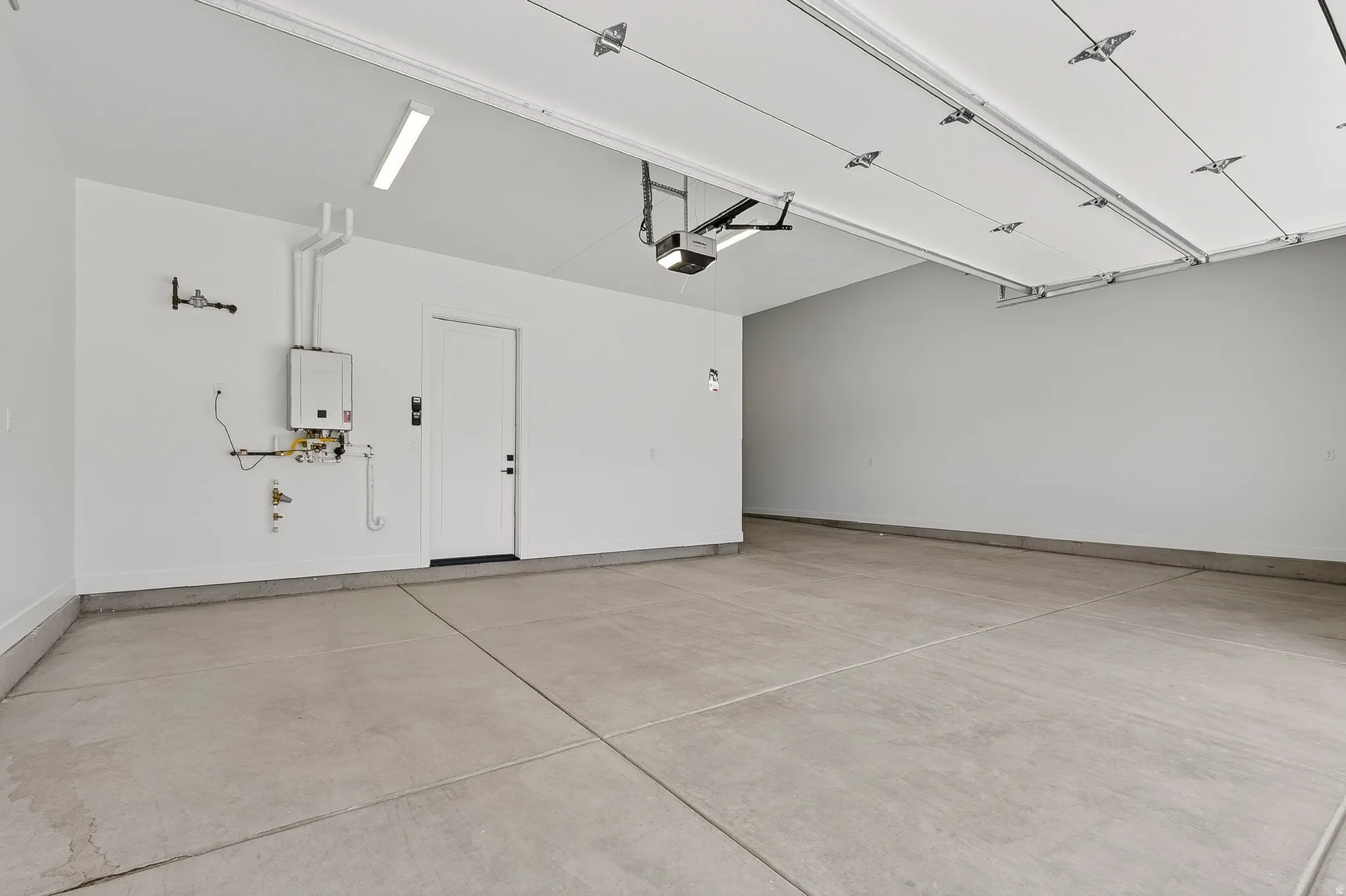 Spacious garage with concrete flooring, tankless water heater, interior access door, and overhead lighting