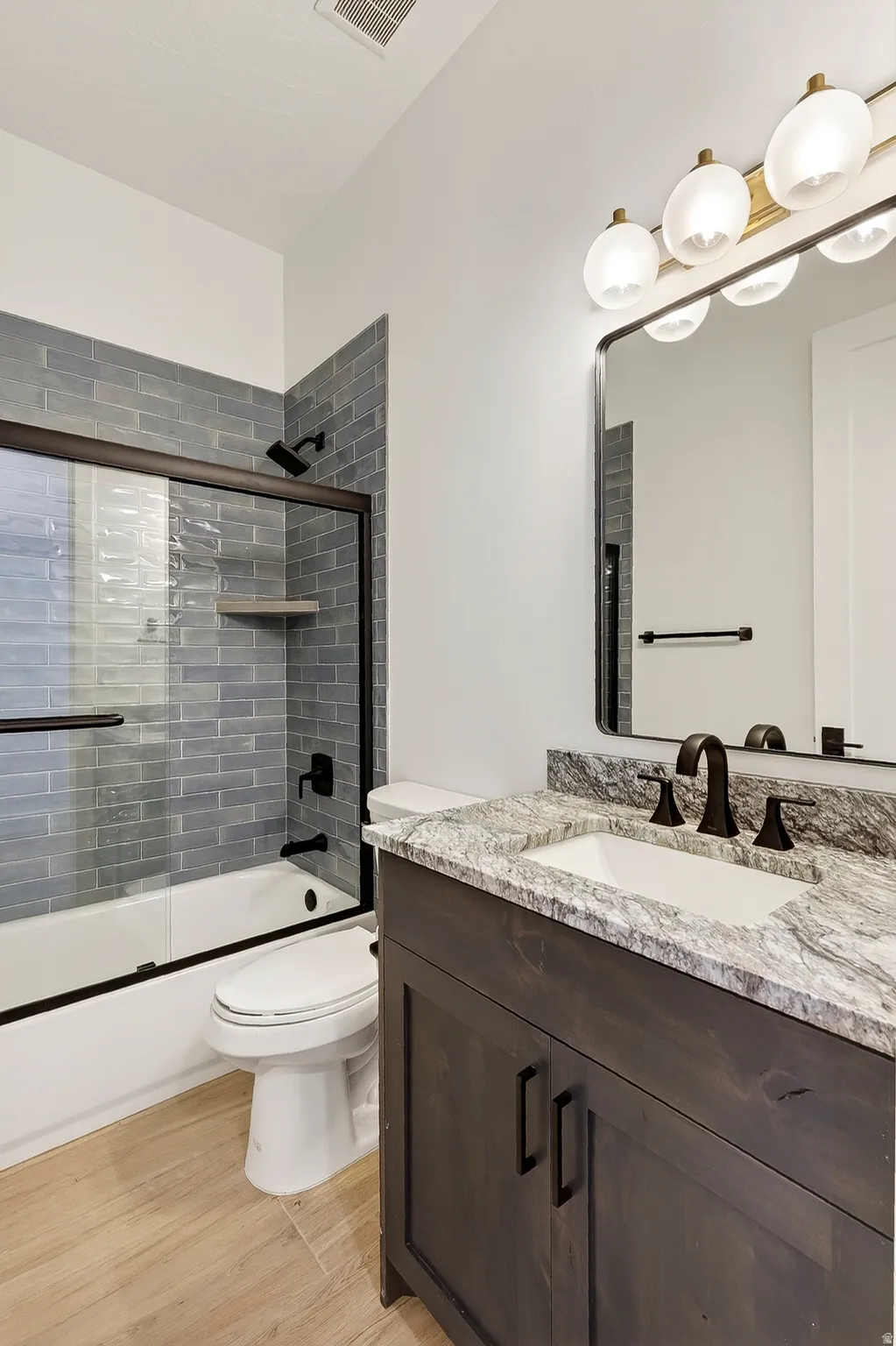 Bathroom featuring a dark wood-finish vanity with a light stone-finish countertop, undermount sink, and matte black fixtures
