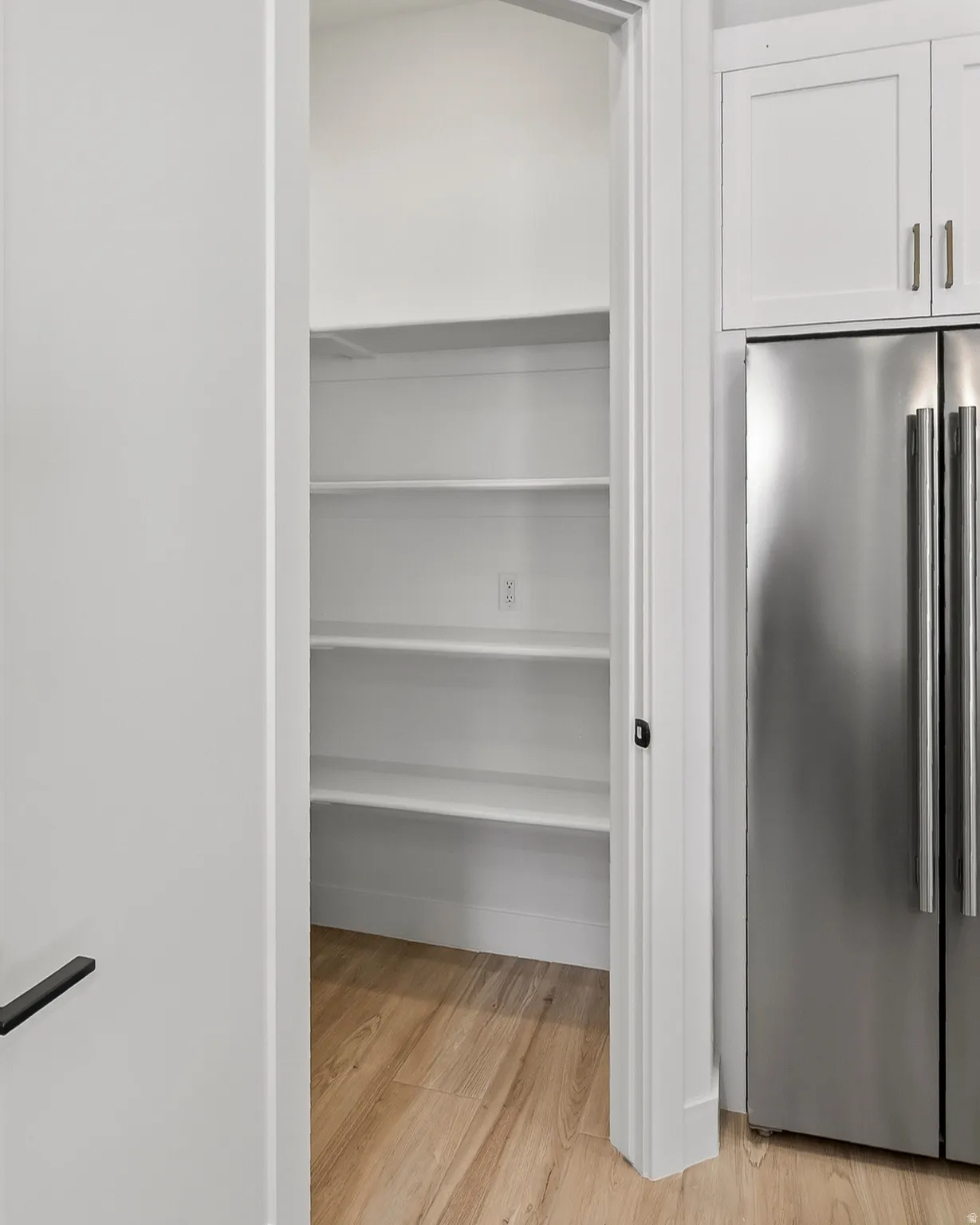 Walk-in pantry featuring multiple white shelving units and wood-finish flooring