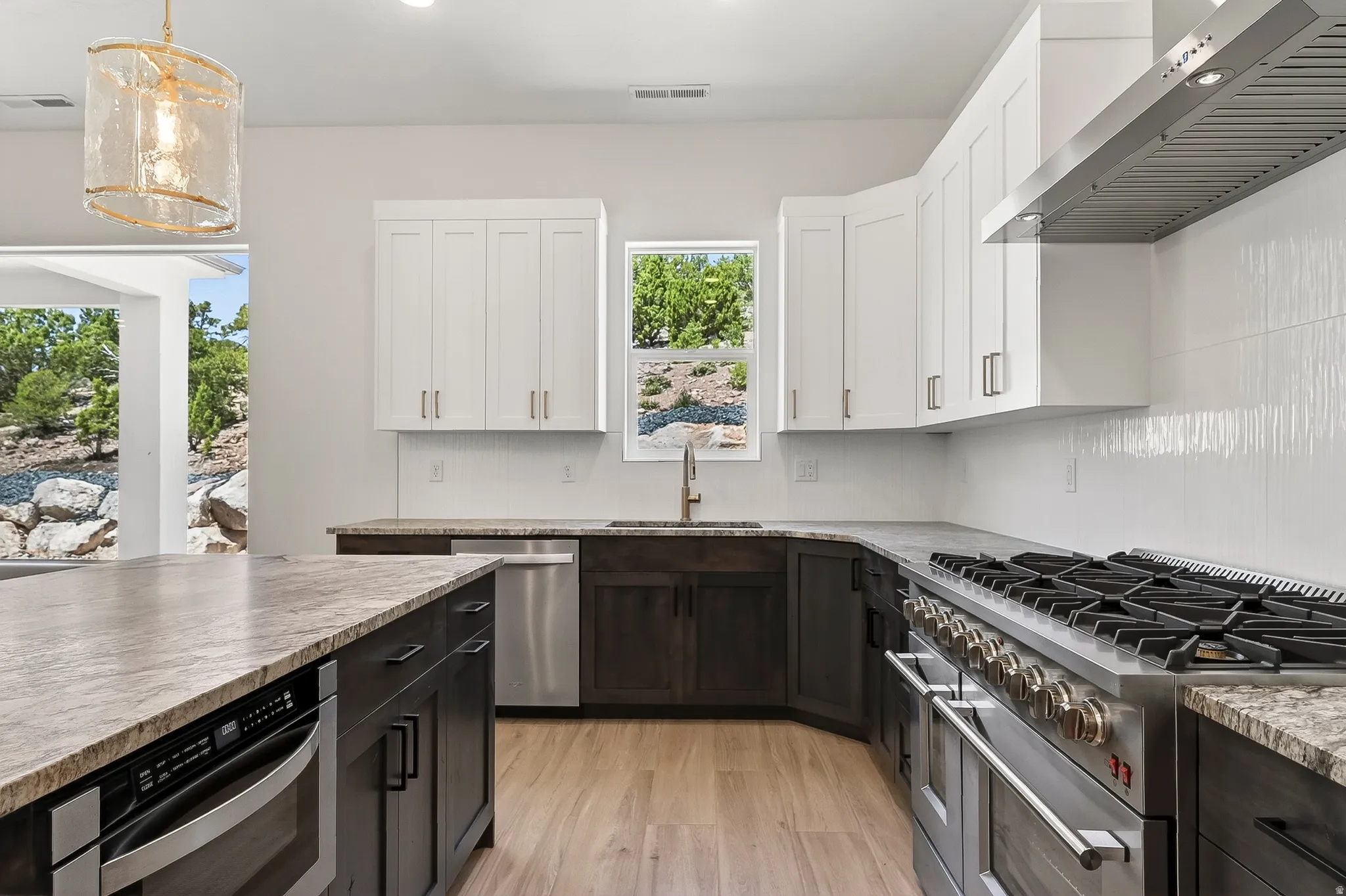Modern kitchen featuring light wood-finish flooring, two-tone cabinetry with dark lower cabinets and white upper cabinets, and a granite-finish countertop