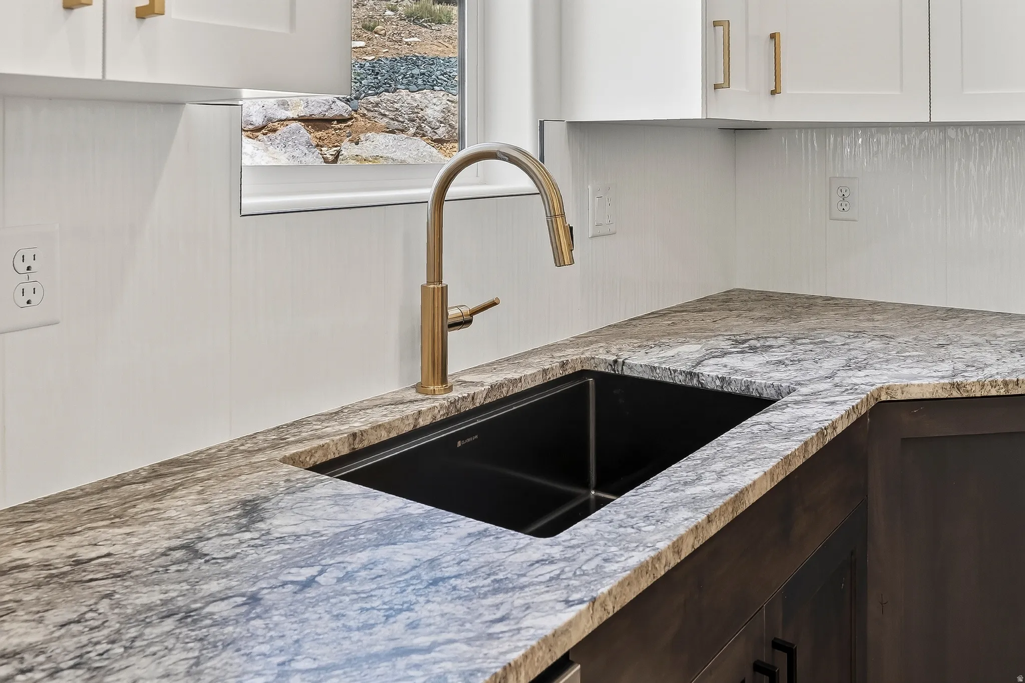 Corner kitchen sink with a gold-tone gooseneck faucet, set into a stone countertop