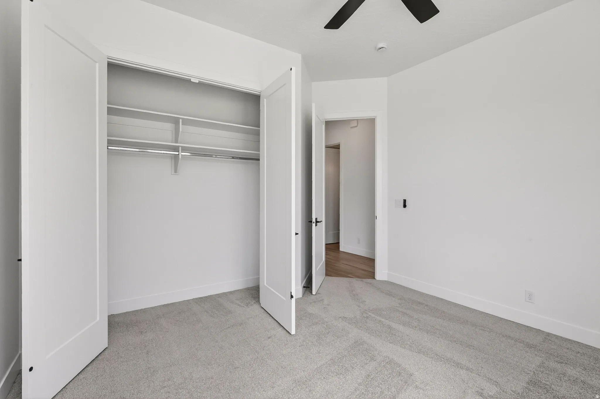 Bedroom featuring light gray carpet, white walls, a ceiling fan with black blades, and a double-door closet with shelving and a hanging rod