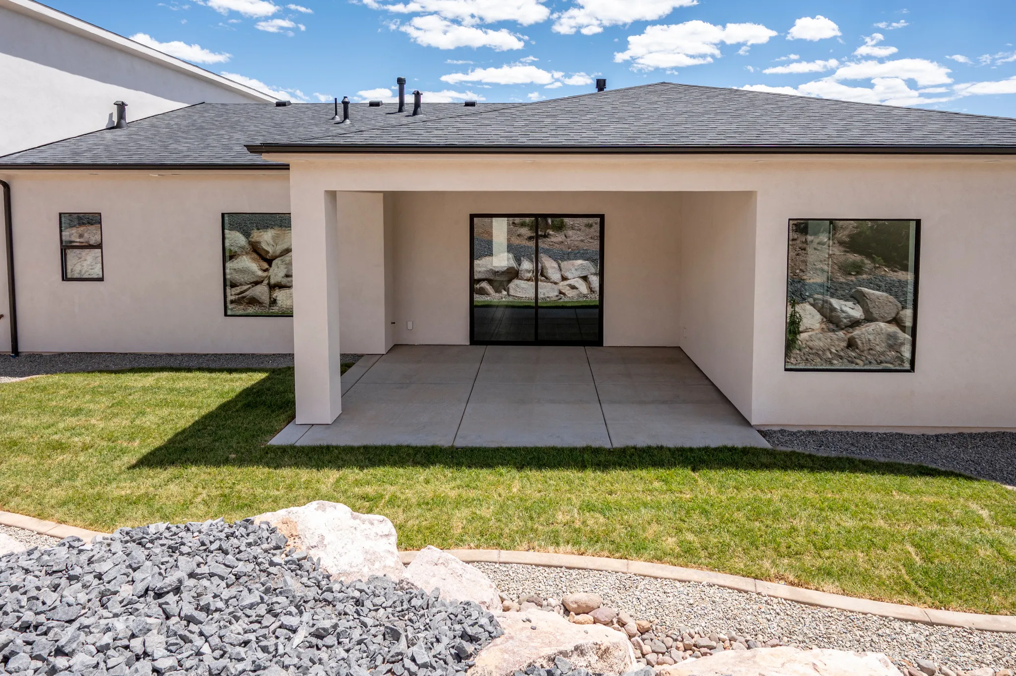 Rear exterior featuring a covered concrete patio, black-framed sliding glass door, and dark-framed windows