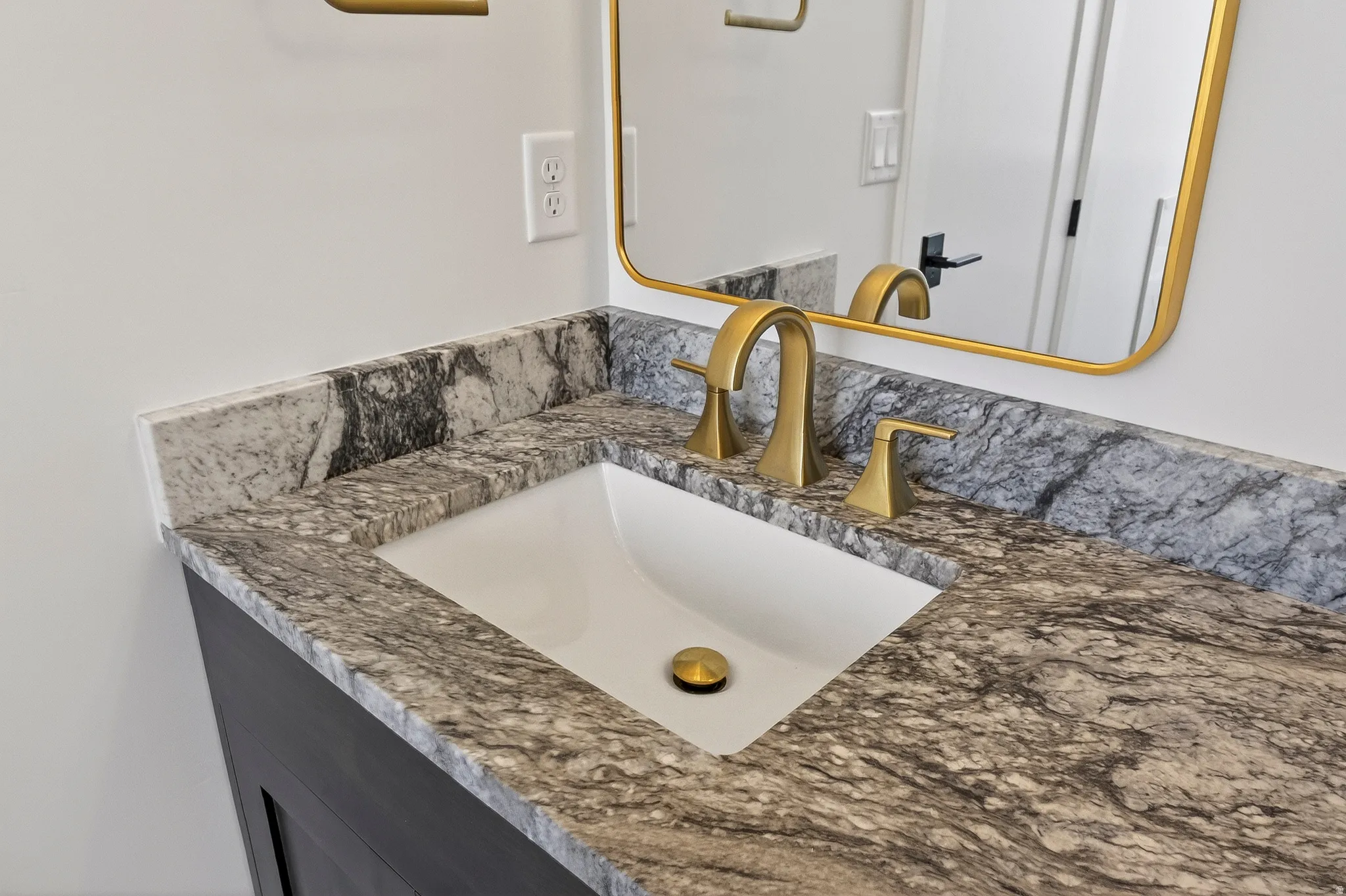 Bathroom vanity featuring a rectangular undermount sink, a patterned stone countertop, and brushed gold hardware