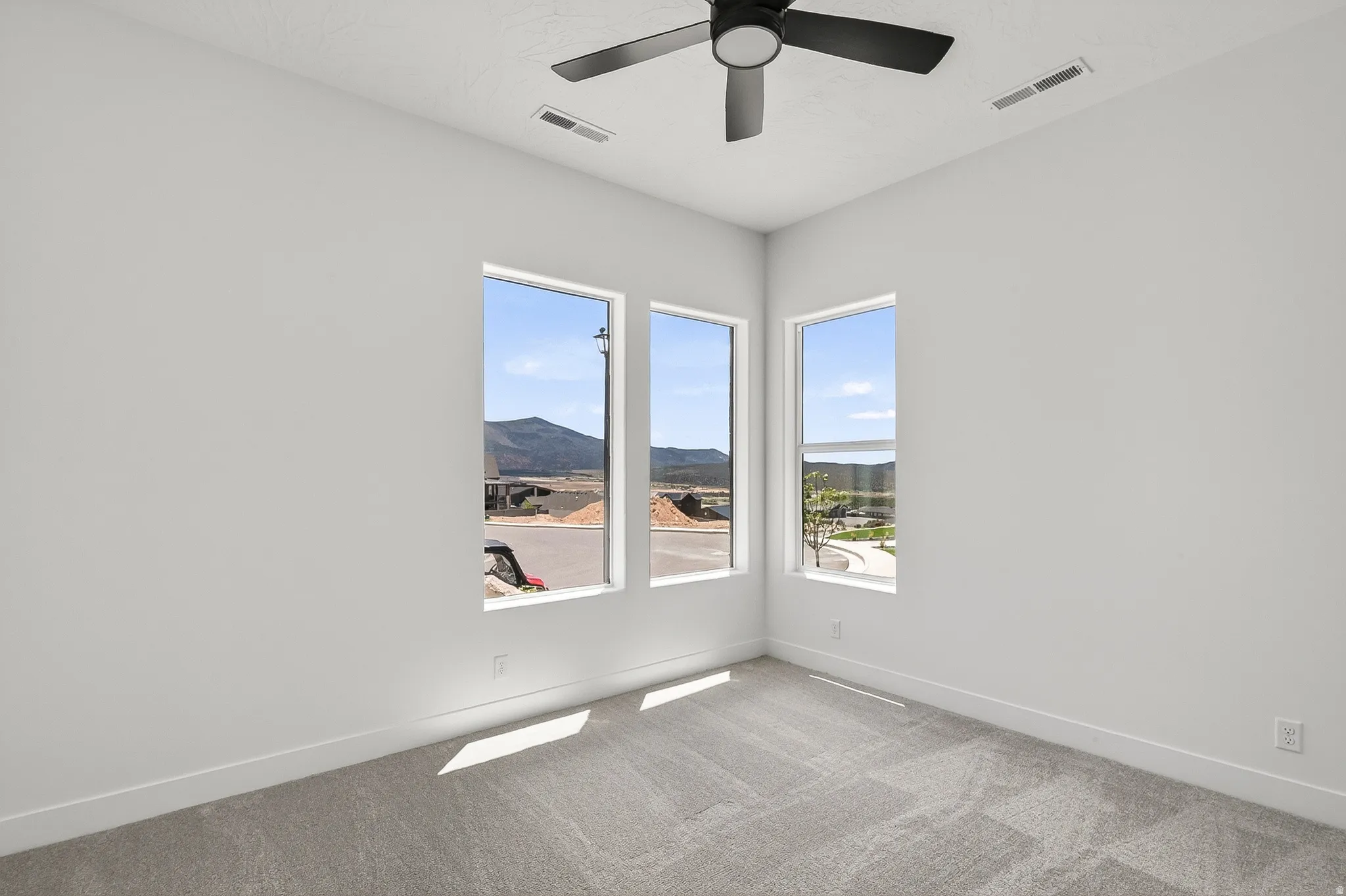 Spacious room featuring three vertical windows, light gray carpeting, and a modern ceiling fan