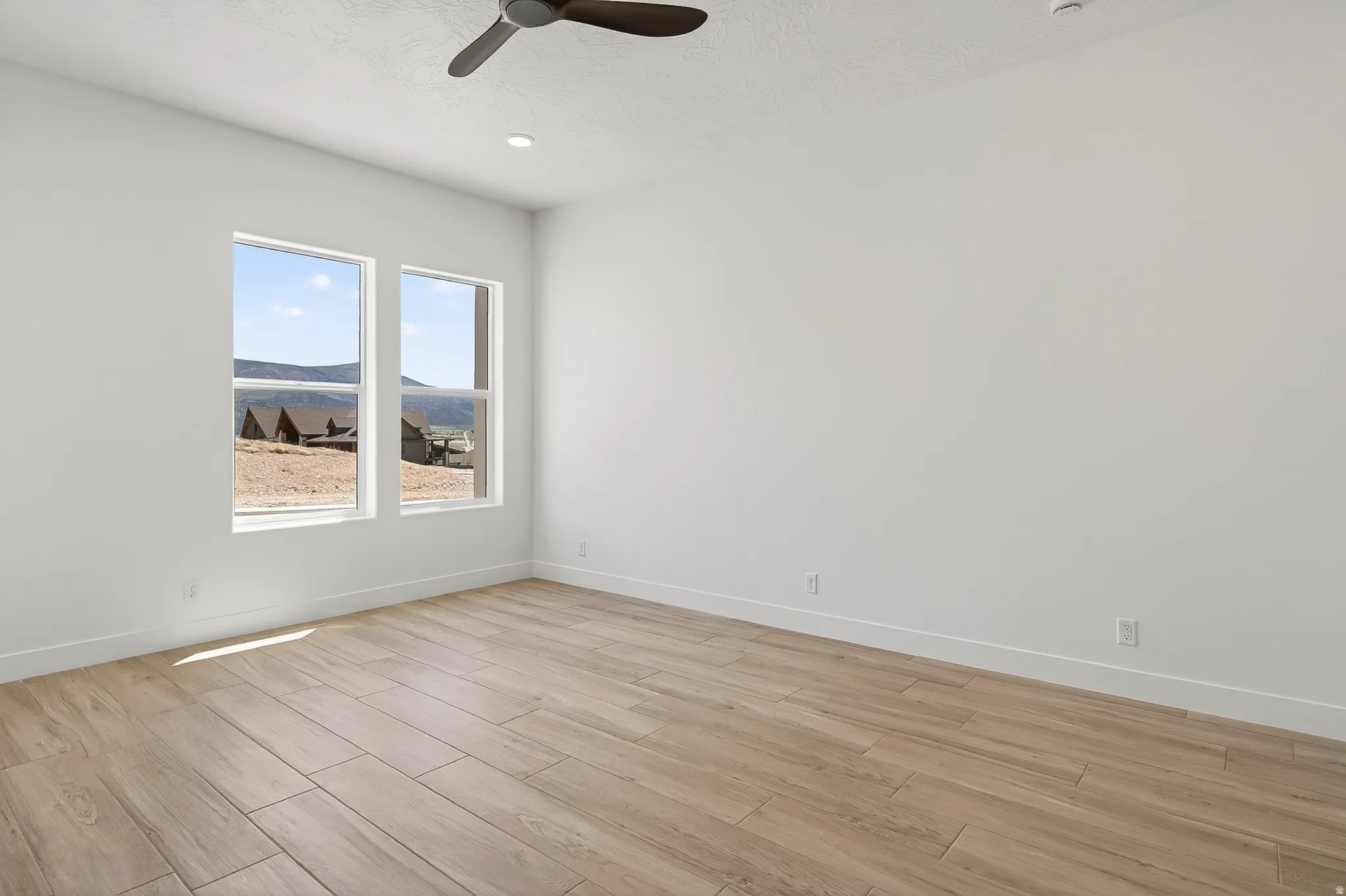 Spacious room with light wood-finish flooring, white walls, and a ceiling fan