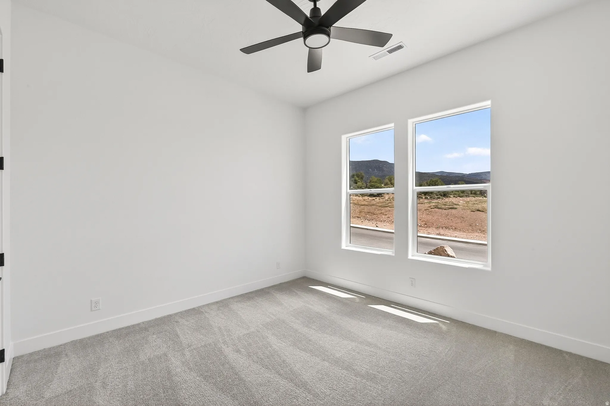 Interior room featuring a contemporary ceiling fan, two large windows, light gray carpeting, crisp white walls, and bright white baseboards