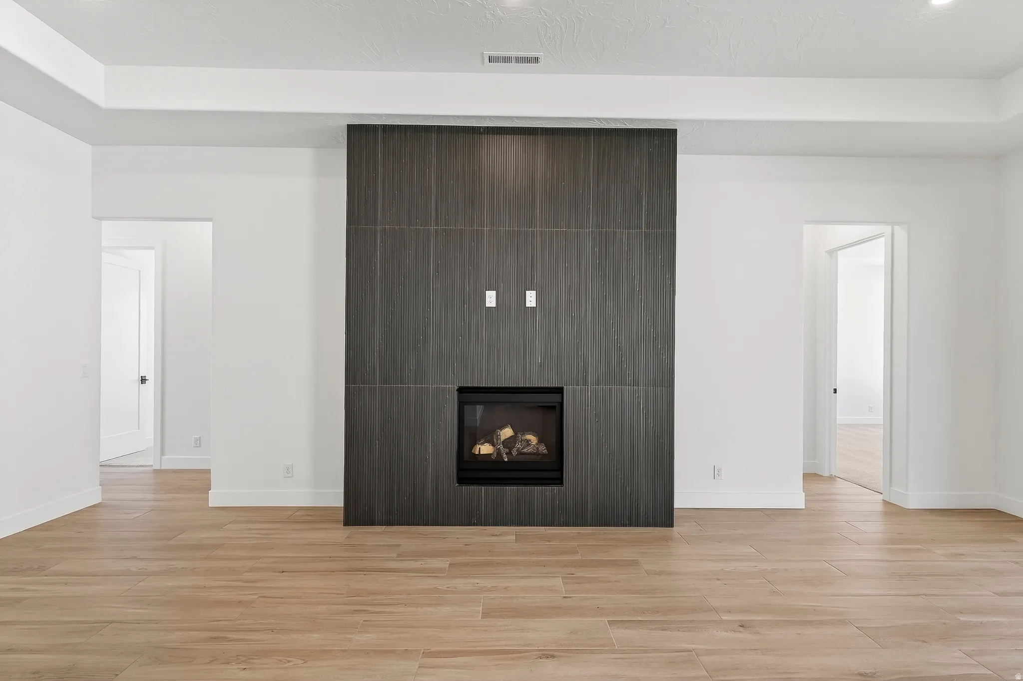 Contemporary linear fireplace with a dark-toned tile surround, complemented by light wood-finish flooring and a tray ceiling