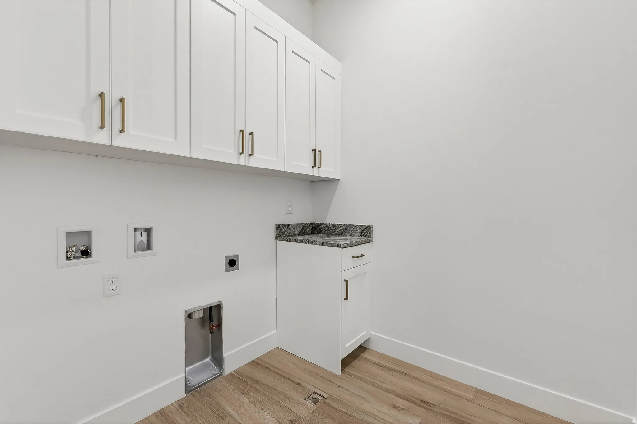 Laundry area featuring white shaker cabinetry, gold-tone hardware, a dark granite countertop, and wood-finish flooring