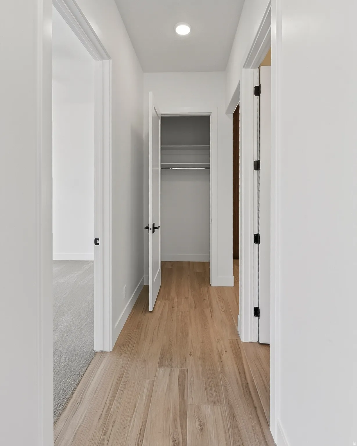 Hallway featuring wood-finish flooring, recessed ceiling lighting, a closet with wire shelving and hanging rod, white walls, and dark hardware