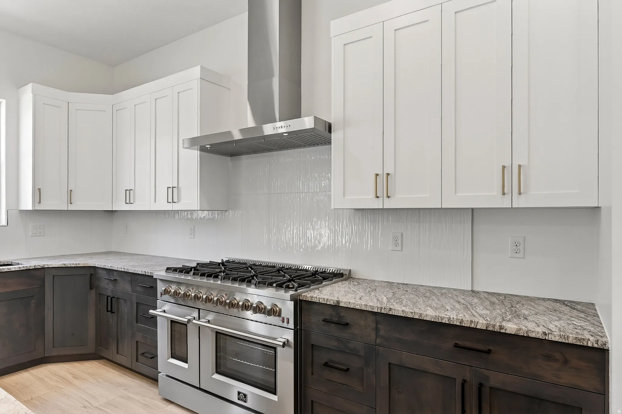 Gourmet kitchen featuring a stainless steel professional-grade range, coordinating stainless steel range hood, white shaker-style upper cabinetry, dark wood-finish lower cabinetry, and light-toned countertops