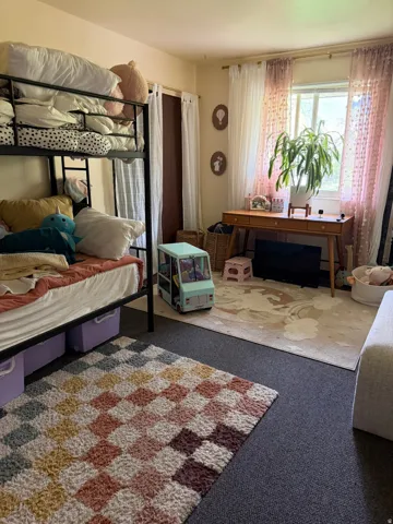 Carpeted bedroom featuring a bunk bed, a window with sheer curtains, and a wooden desk