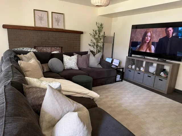 Living area featuring a brick fireplace with a wood mantle, complemented by a light-toned patterned area rug