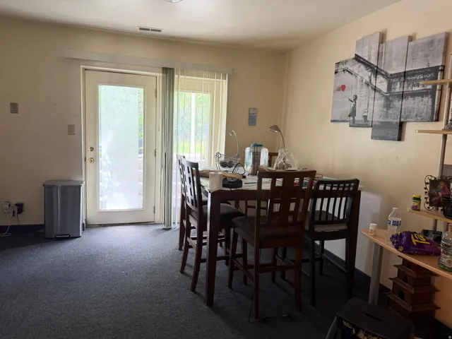 Dining area featuring dark carpeting, a light beige wall color, and a white sliding glass door with vertical blinds