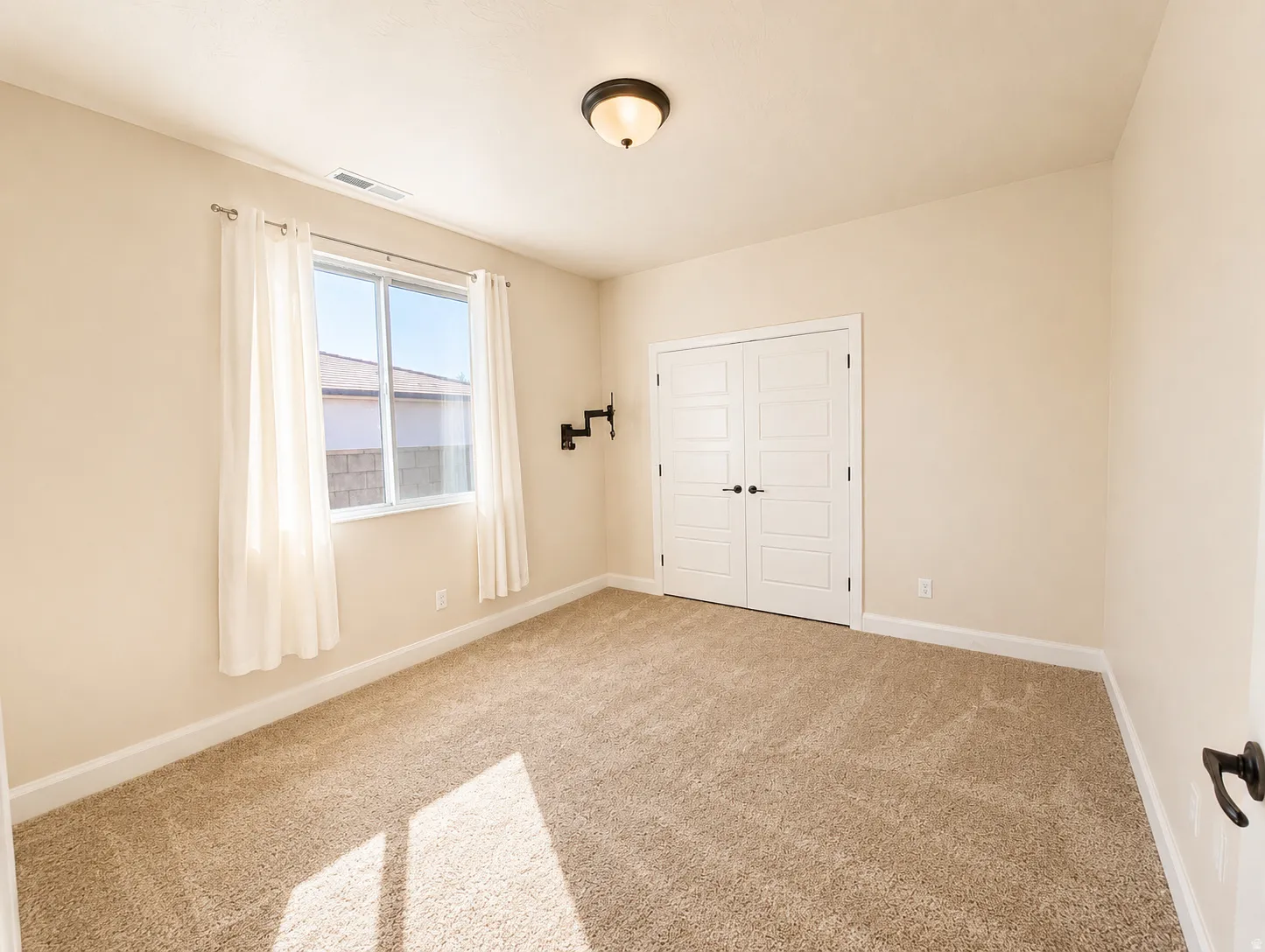 Carpeted room featuring a double-pane window with sheer curtains, a flush-mount ceiling light, and white double bifold doors