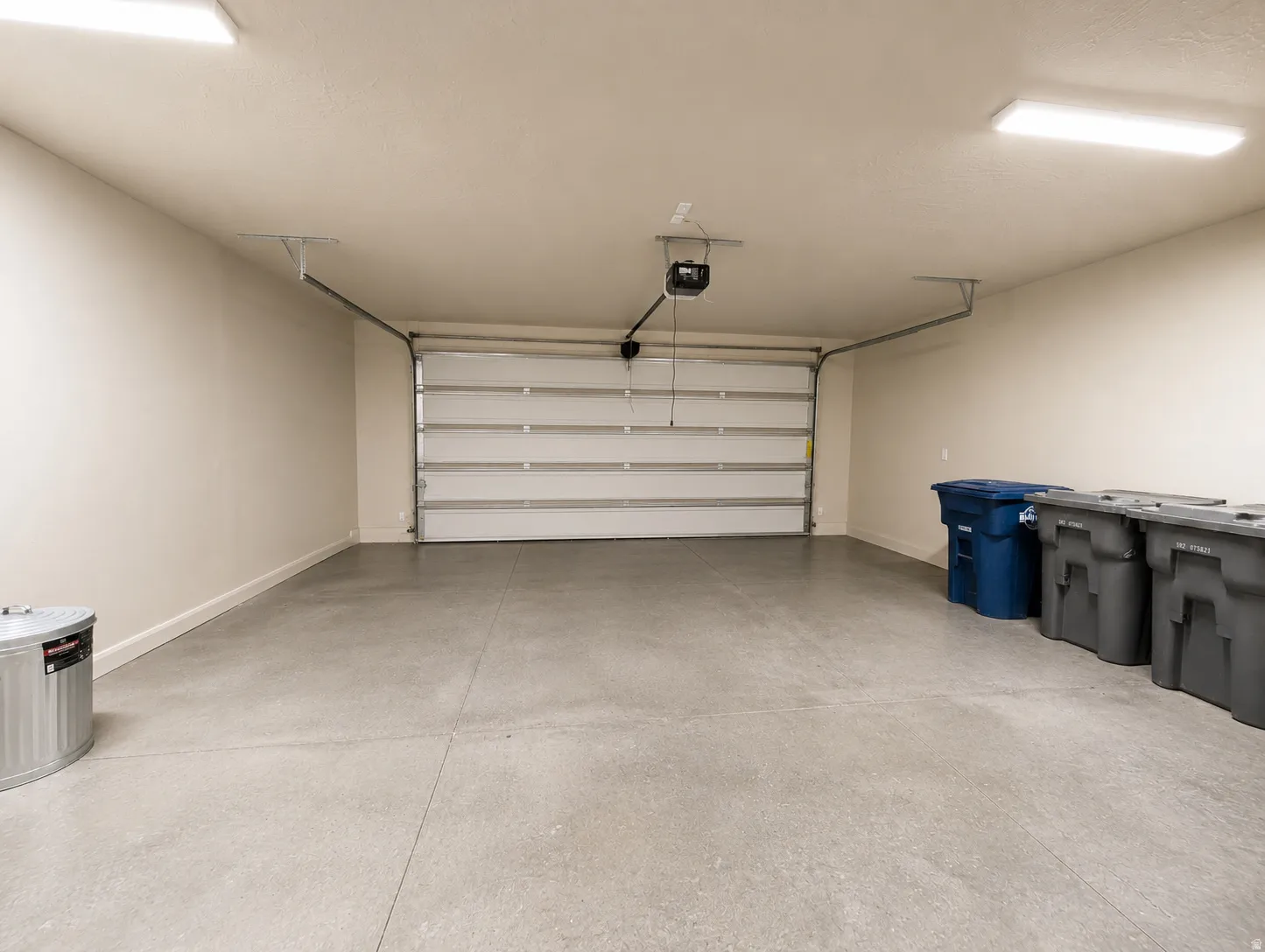 Spacious garage featuring a concrete floor, light-toned walls, a white sectional garage door, and ceiling-mounted lighting fixtures