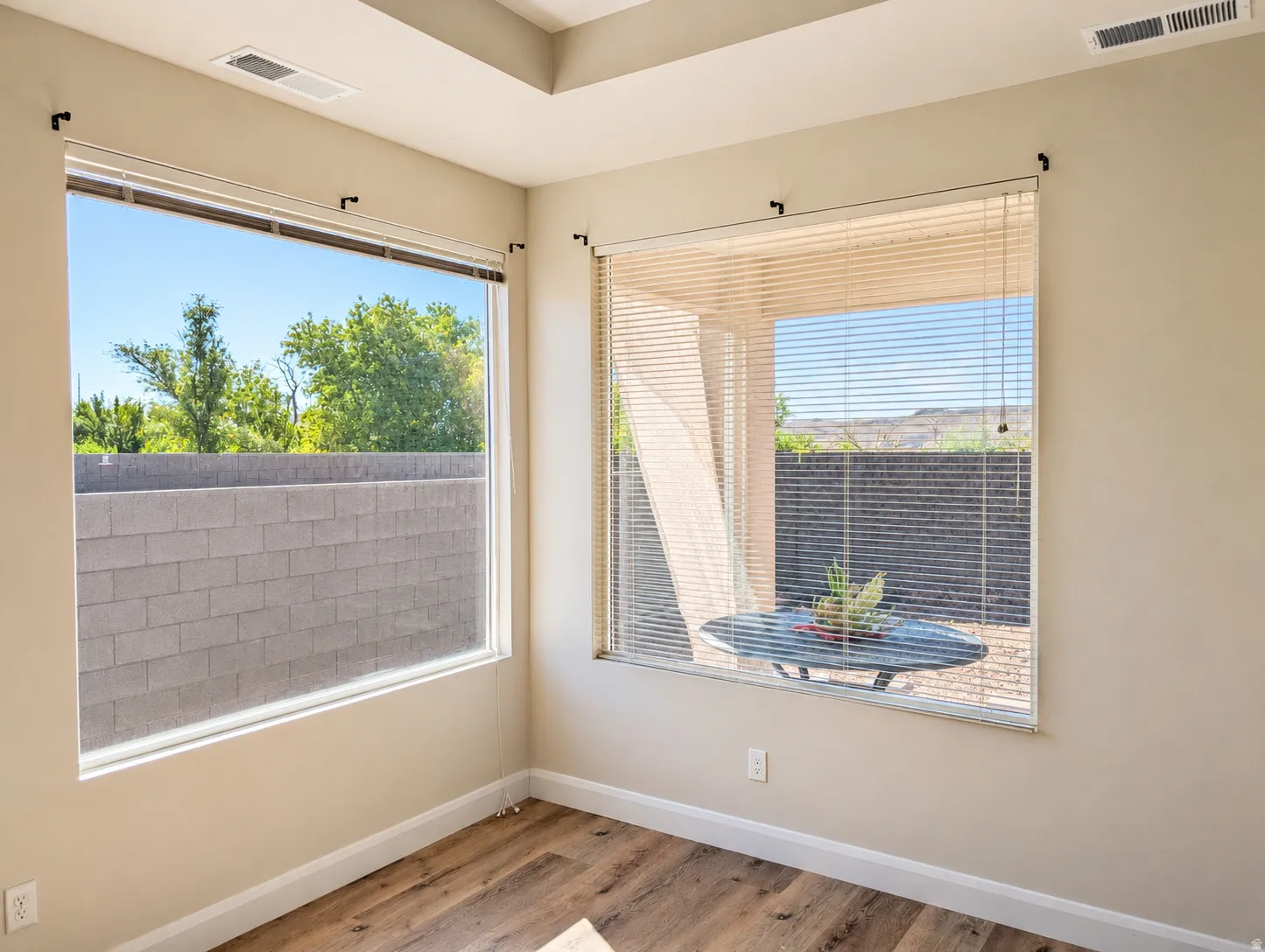 Room featuring wood-finish flooring, two large windows with blinds, and light-toned walls