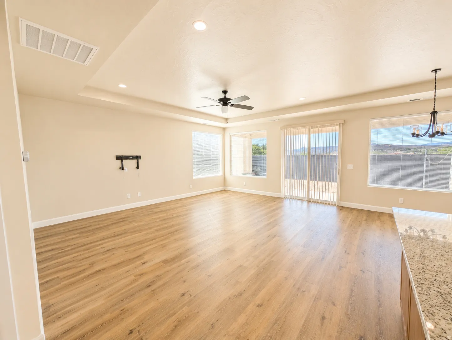 Spacious open-concept room featuring wood-finish flooring, abundant natural light from multiple windows, and a tray ceiling with recessed lighting