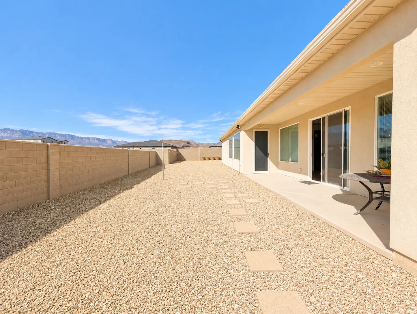 Spacious exterior featuring a rock-covered yard, concrete patio, block wall perimeter, and sliding glass doors