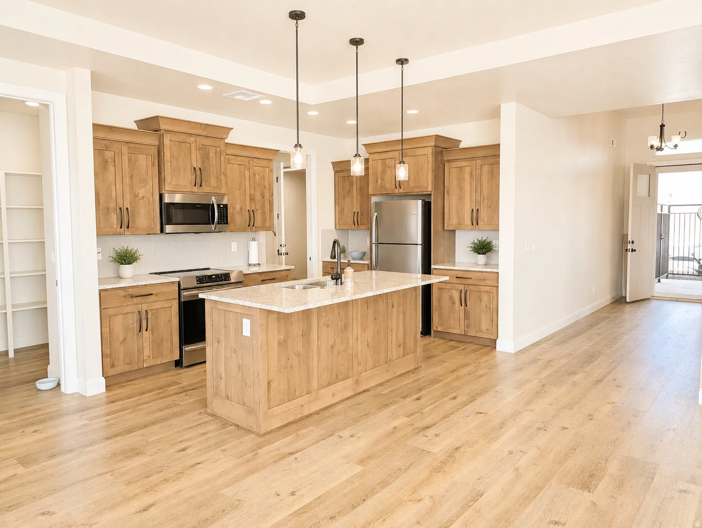 Open-concept kitchen with wood-finish flooring, light wood cabinetry, stainless steel appliances, and a central island with a light-colored countertop
