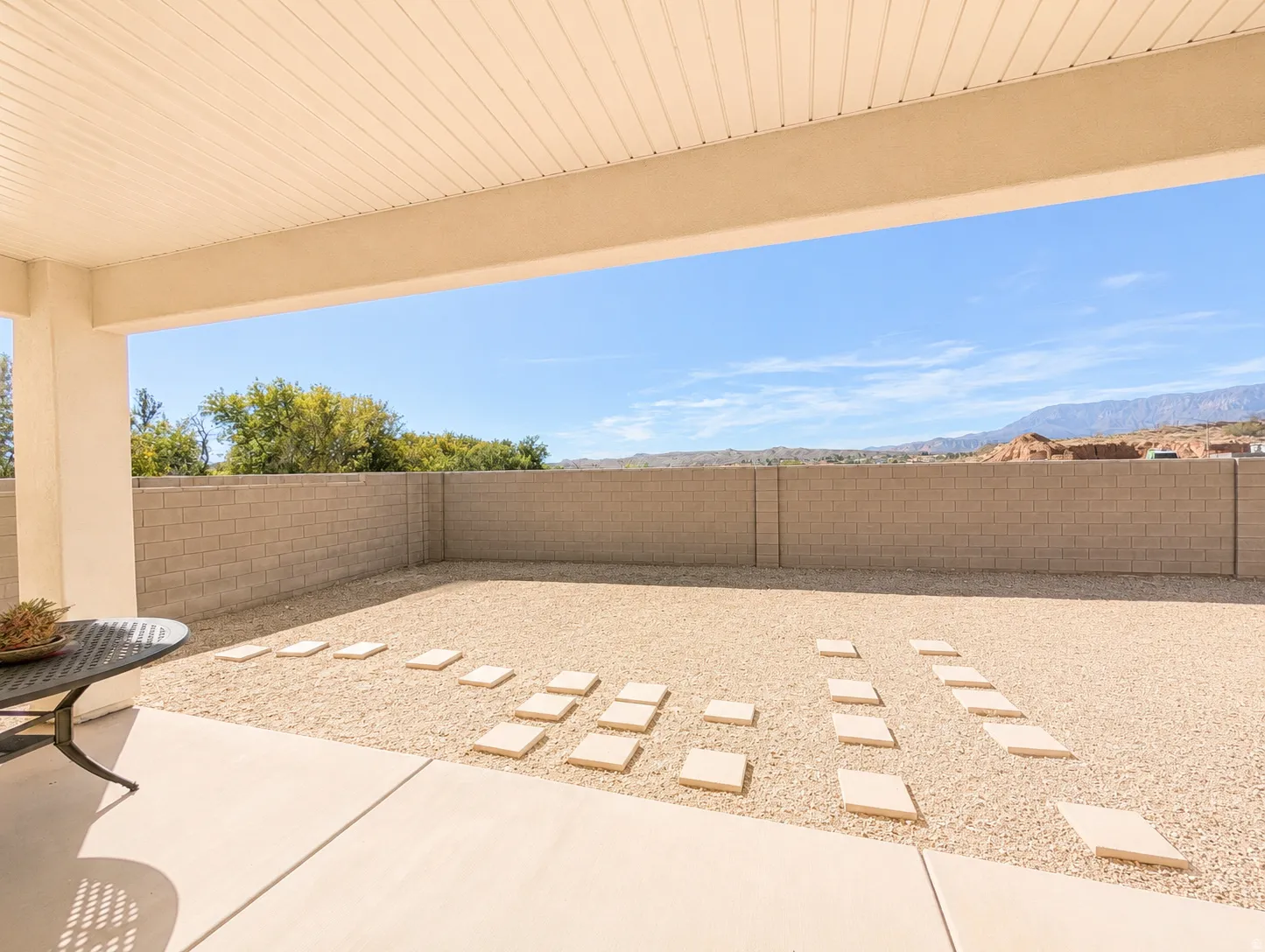 Covered patio with concrete flooring, extending to a gravel yard featuring large square stepping stones