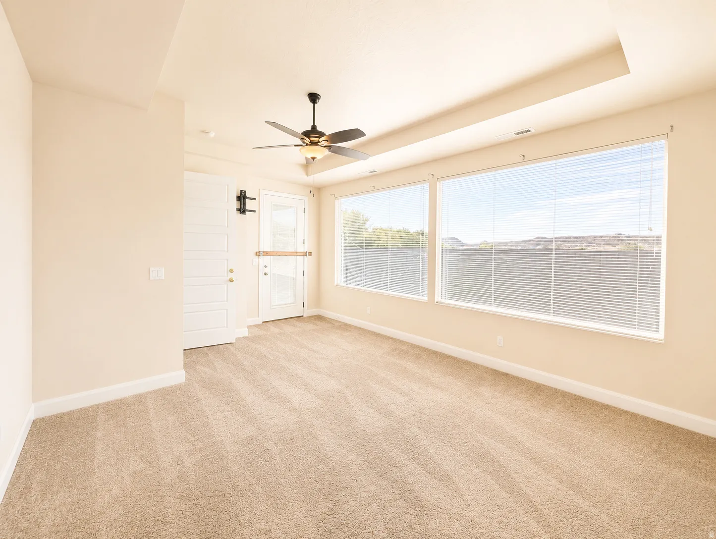 Expansive room featuring multiple windows with horizontal blinds, a tray ceiling, and a ceiling fan with integrated lighting
