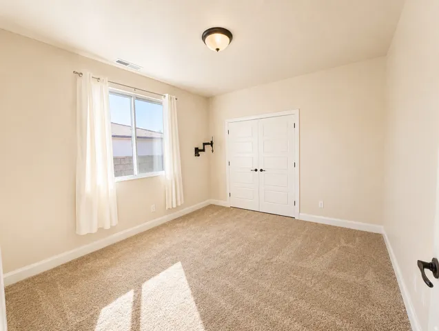 Carpeted room featuring a double-pane window with sheer curtains, a flush-mount ceiling light, and white double bifold doors