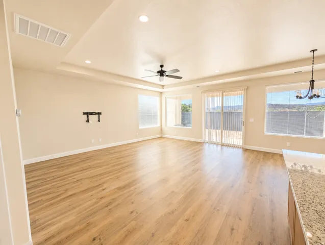 Spacious open-concept room featuring wood-finish flooring, abundant natural light from multiple windows, and a tray ceiling with recessed lighting