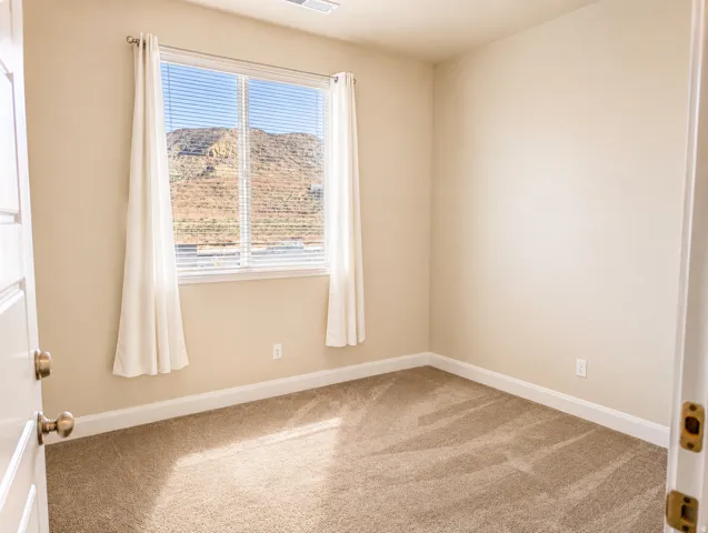 Neutral-toned carpeted room featuring a large window with white blinds and drapes
