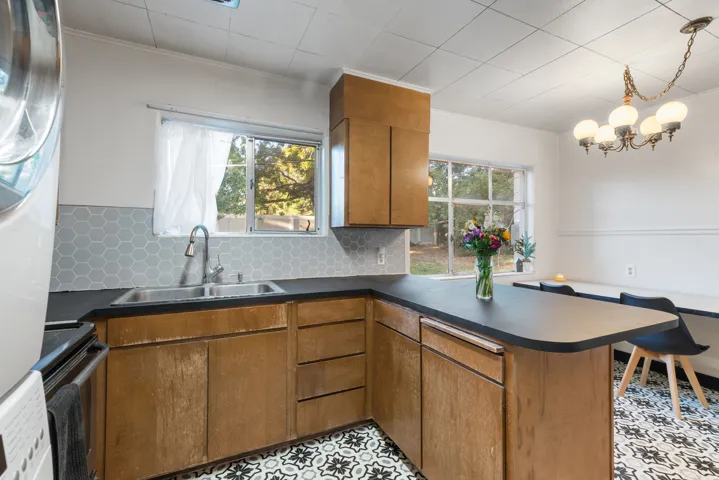 Kitchen area featuring wood cabinetry, dark countertops, a double basin stainless steel sink, and a gray hexagonal tile backsplash