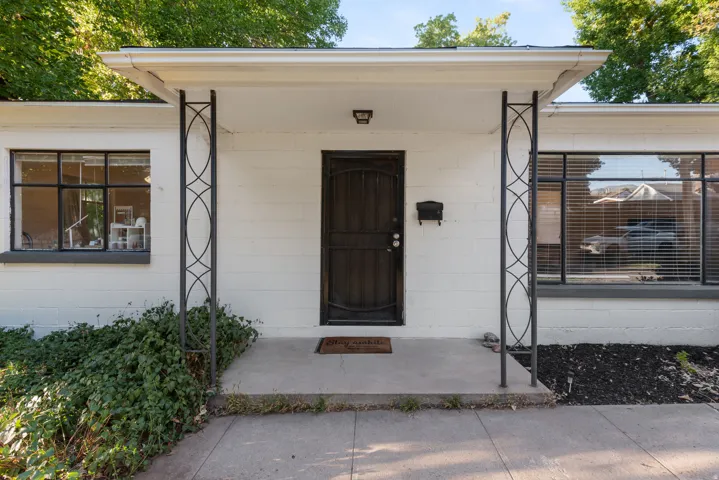 White exterior featuring a dark entry door, two decorative metal support columns, and large windows with black trim