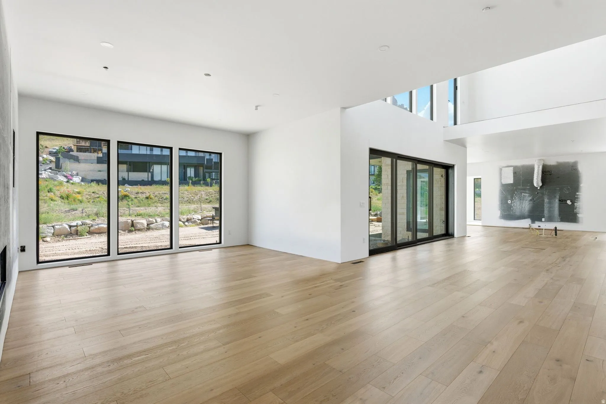 Spacious interior featuring light wood-finish flooring, white walls, and multiple large windows with black frames