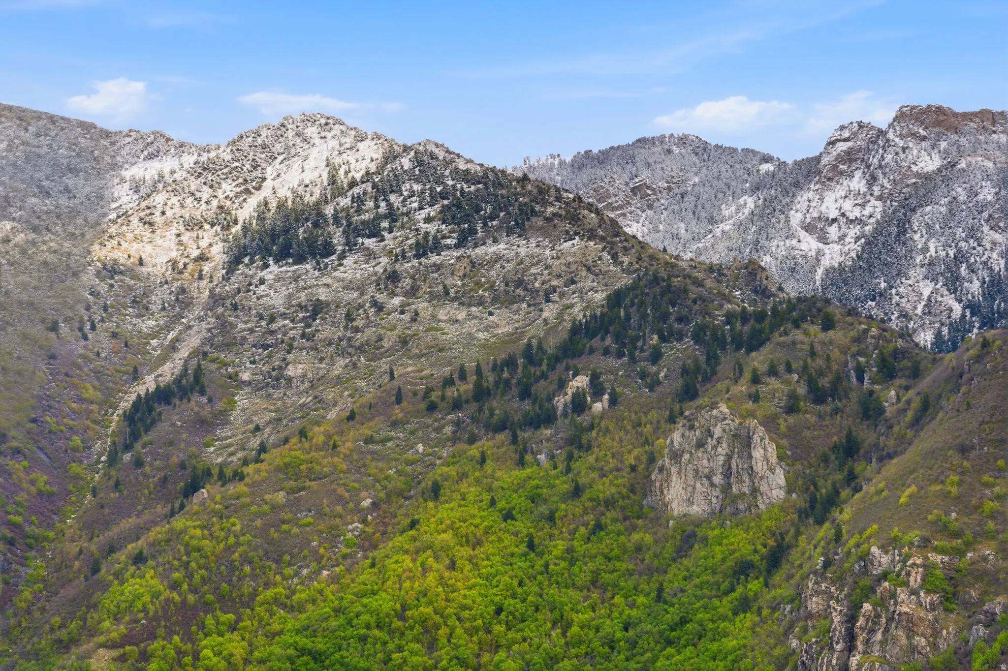 Mountainous landscape featuring varied terrain, including snow-capped peaks, verdant hillsides, and exposed rock formations
