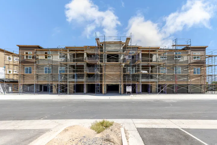 Multi-story structure under construction featuring scaffolding, multiple window openings, and a paved parking area
