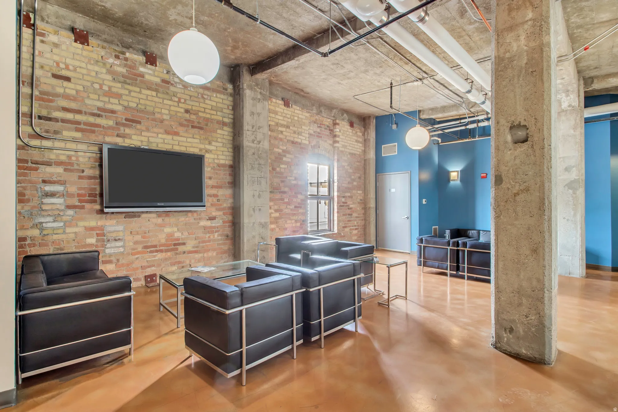 Exposed brick wall with mounted television, concrete ceiling, and industrial-style pendant lighting