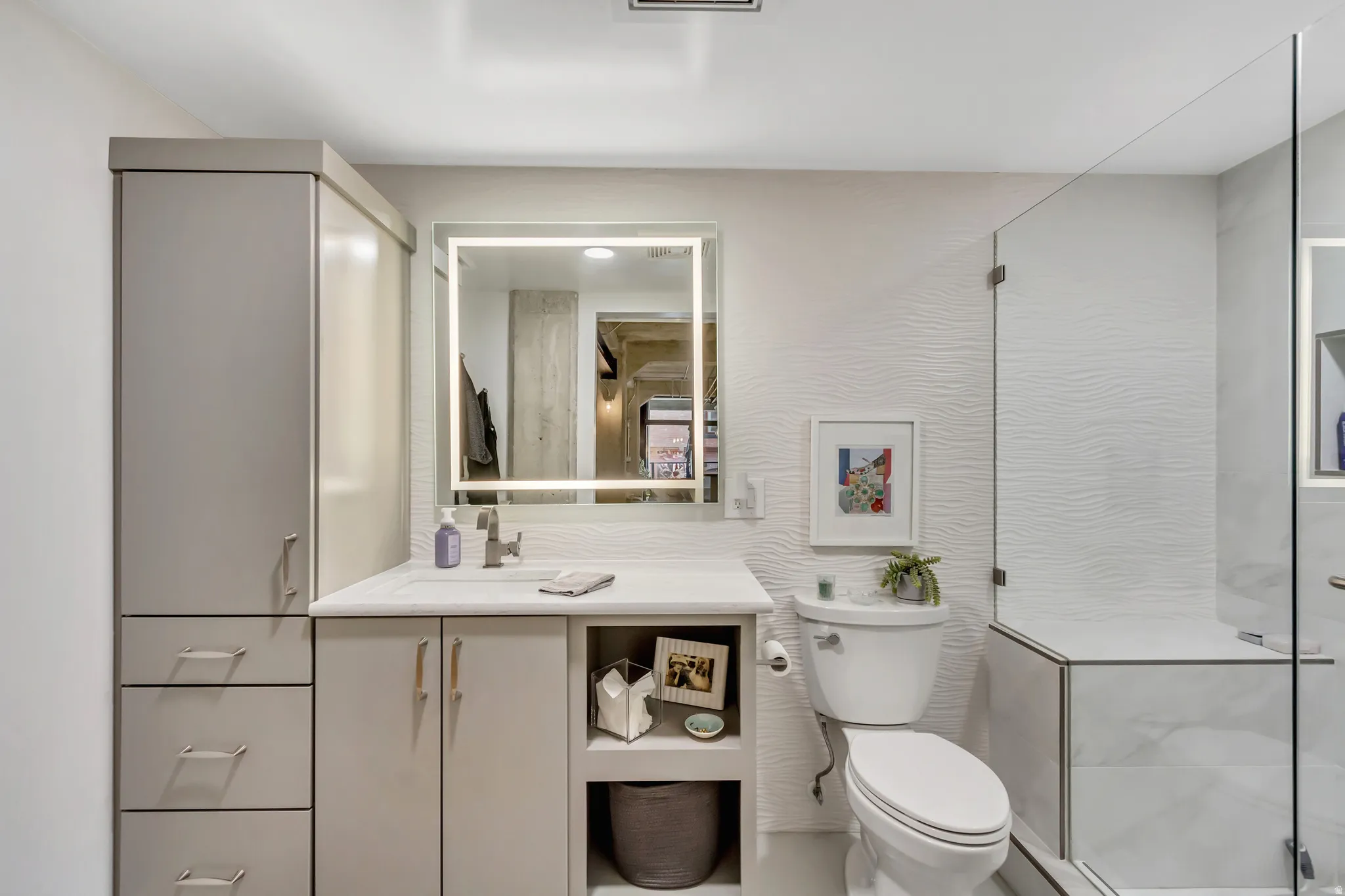Bathroom featuring a frameless glass shower enclosure, a vanity with integrated sink, and an illuminated mirror