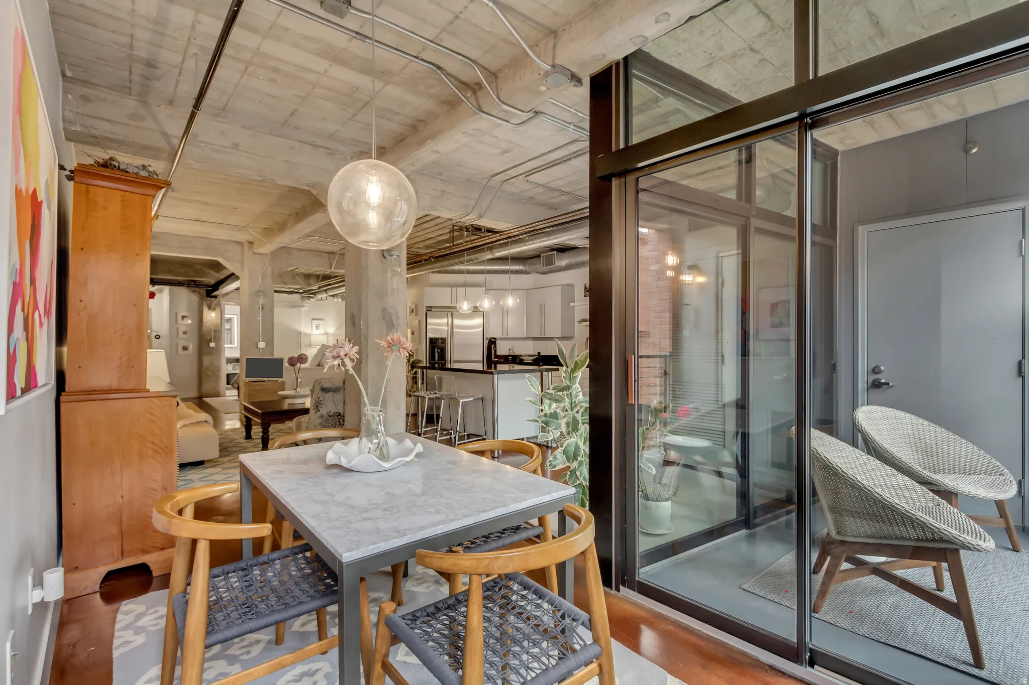 Open-concept living area featuring a concrete ceiling with exposed conduit, a dining area with a stone-finish table, and a glass-enclosed patio