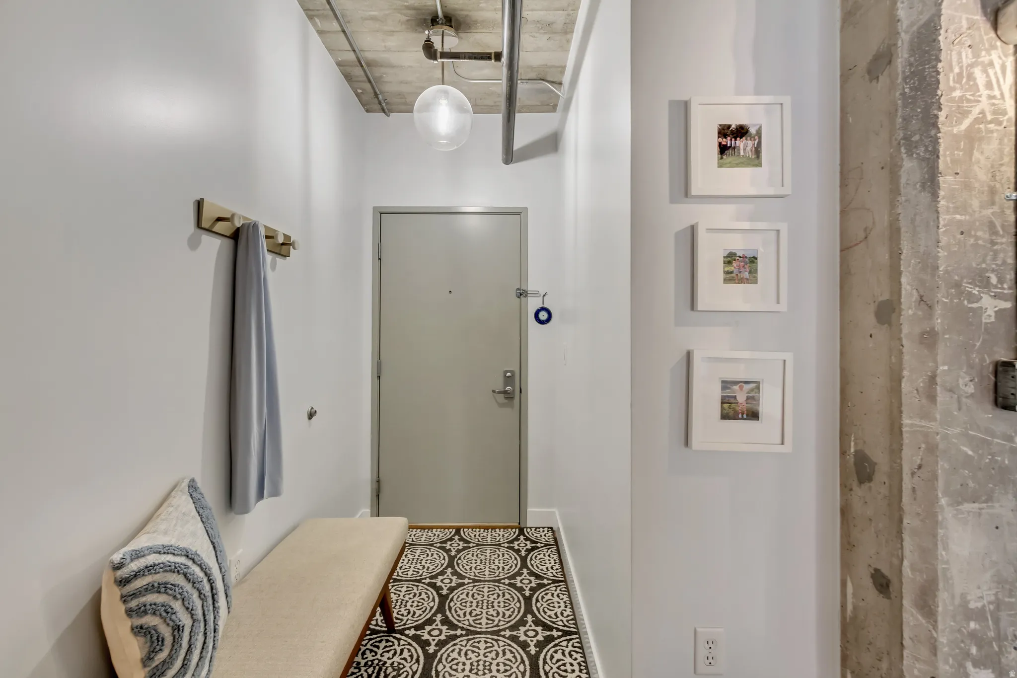 Entryway featuring a patterned floor tile, exposed concrete ceiling with industrial piping, a flush-mounted spherical light fixture, and a solid entry door