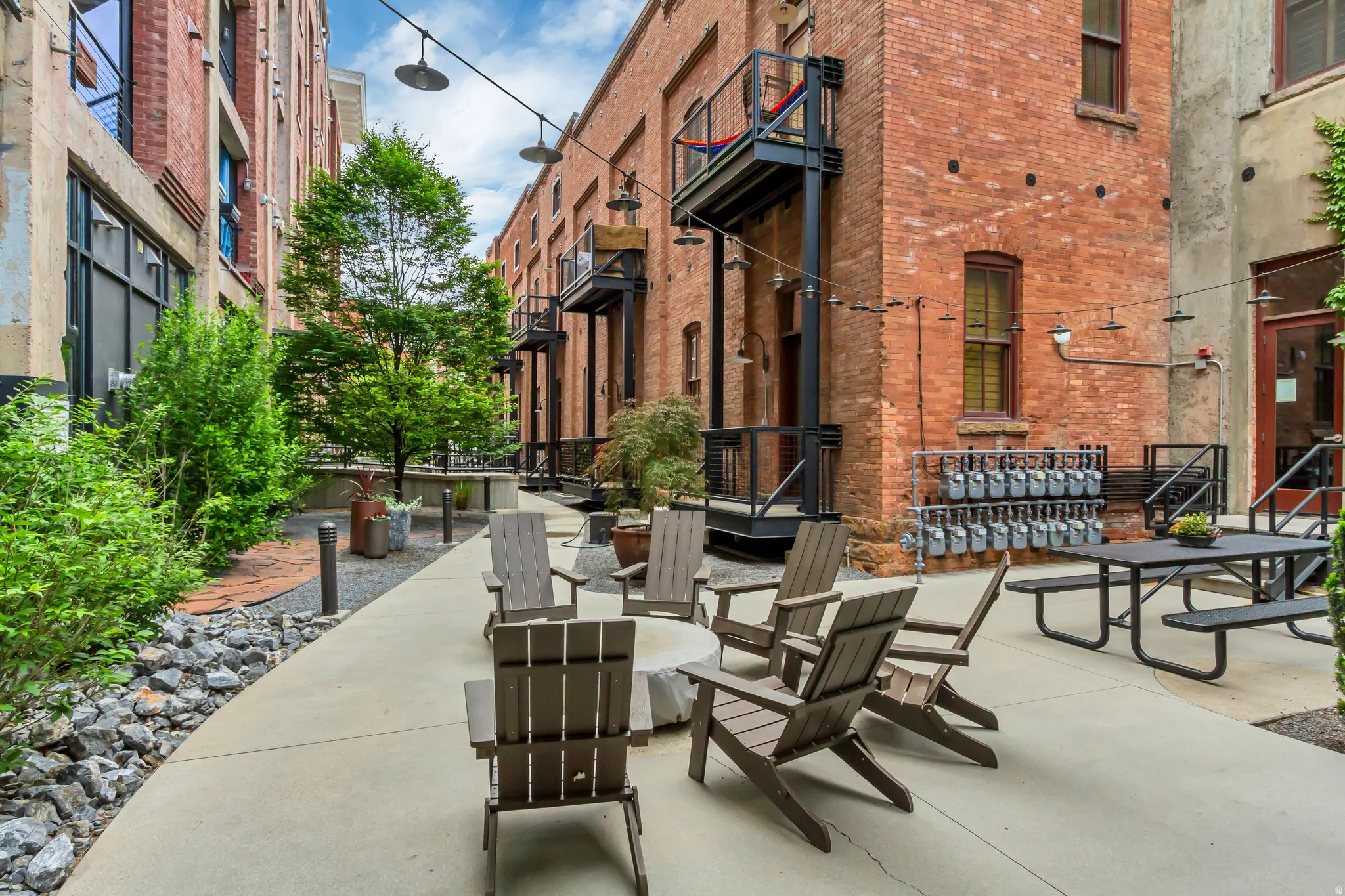Paved outdoor patio featuring a fire pit, Adirondack chairs, and a picnic table