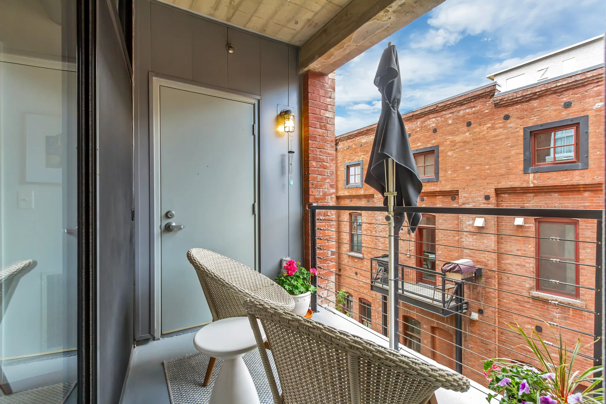 Private balcony featuring a metal cable railing, concrete flooring, and an exterior light fixture