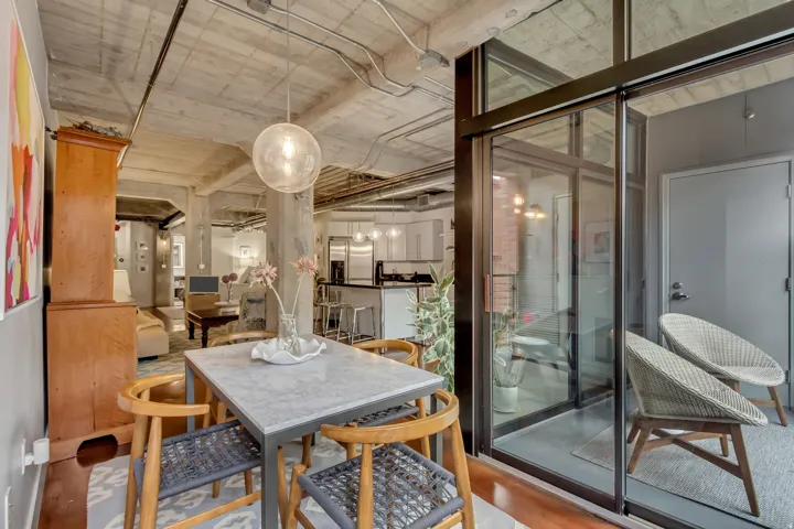 Open-concept living area featuring a concrete ceiling with exposed conduit, a dining area with a stone-finish table, and a glass-enclosed patio