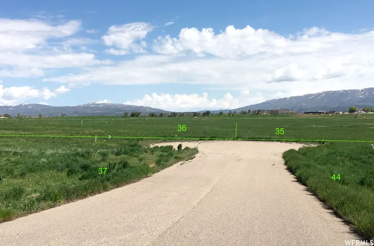 Expansive undeveloped land featuring a paved road entrance, green fields, and distant mountains