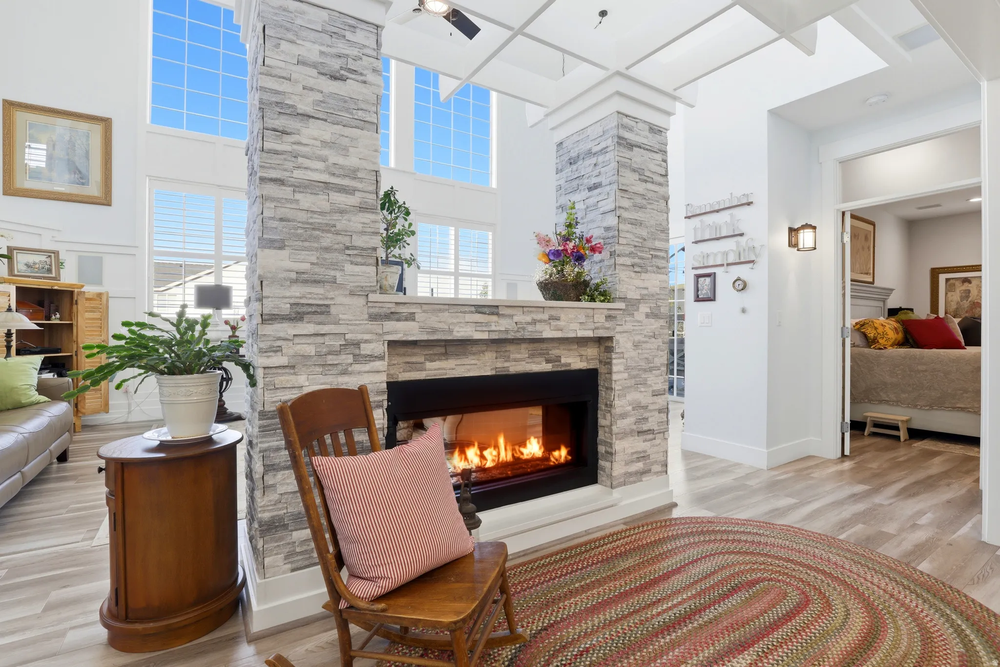 Floor-to-ceiling stone-faced fireplace with a wide hearth, high ceilings, and extensive windowing featuring natural light, wood-finish flooring, and bright white wall finishes