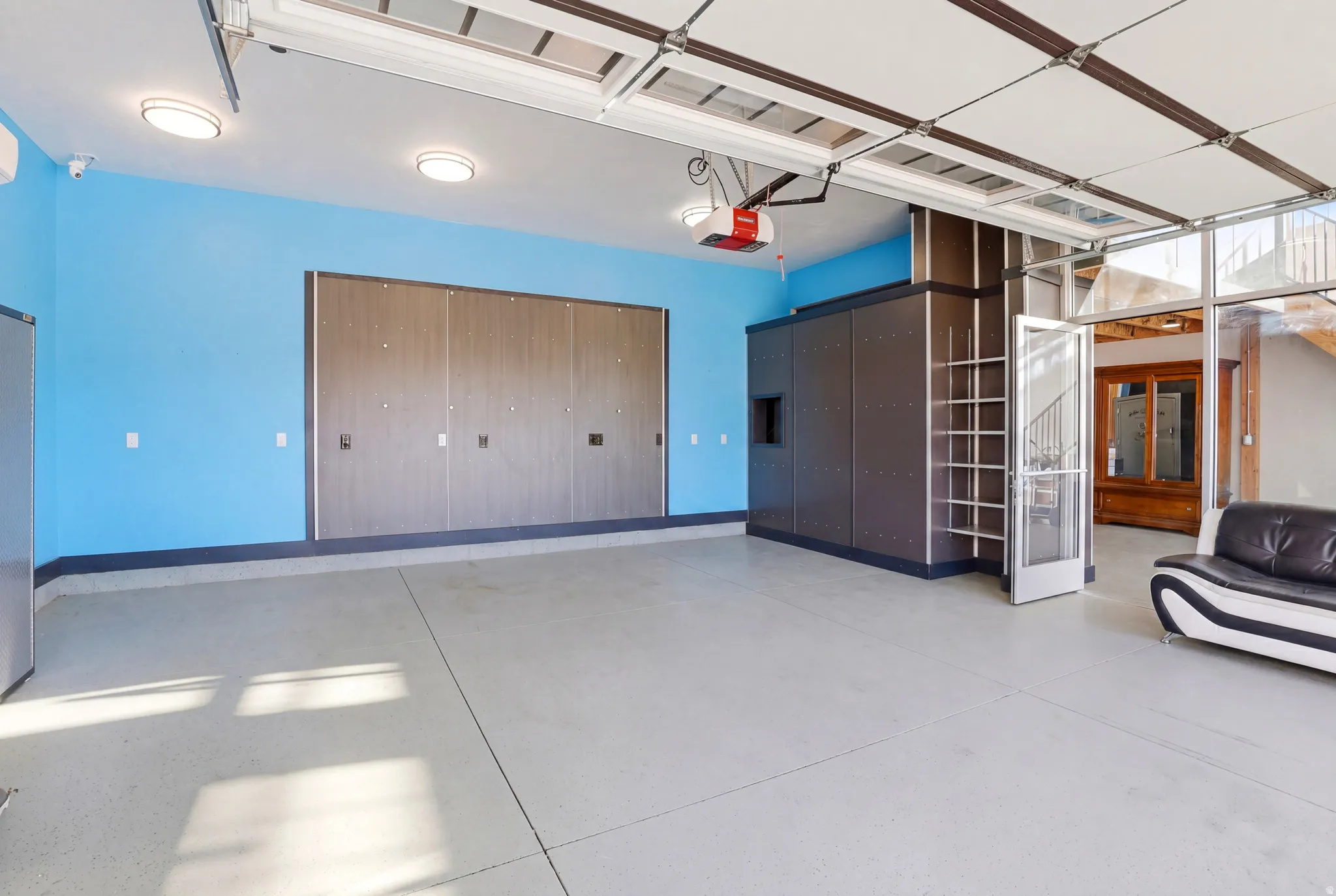 Spacious garage featuring light blue walls, a concrete floor, overhead lighting, an automatic garage door opener, and a built-in storage system with shelving