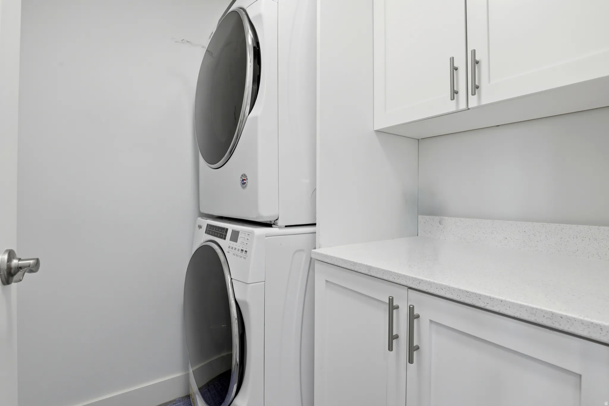 Laundry area featuring stackable appliances, white cabinetry, a light-toned countertop, and brushed nickel hardware