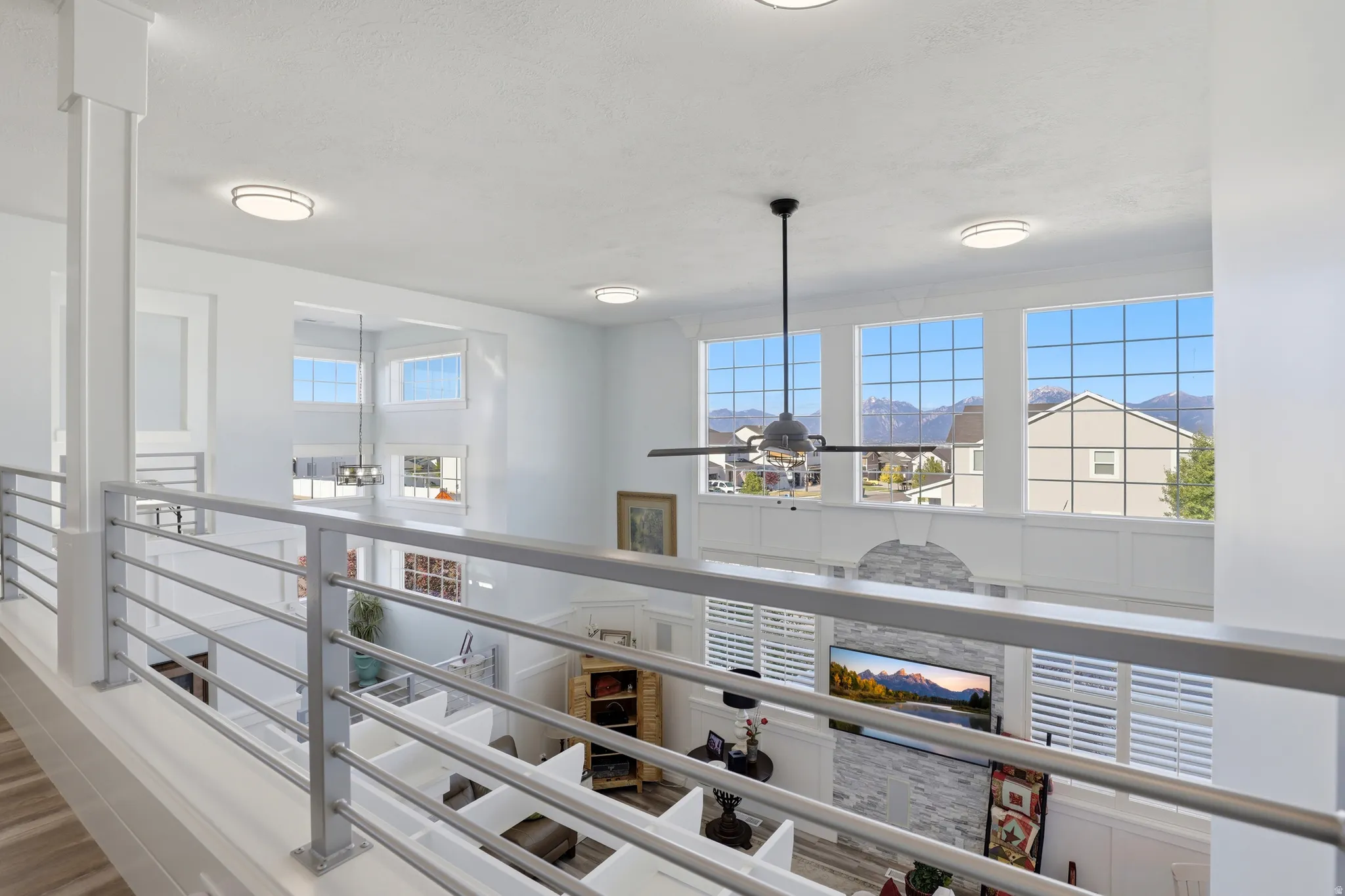 Open loft overlooking a living area with high ceilings, large windows, and a ceiling fan