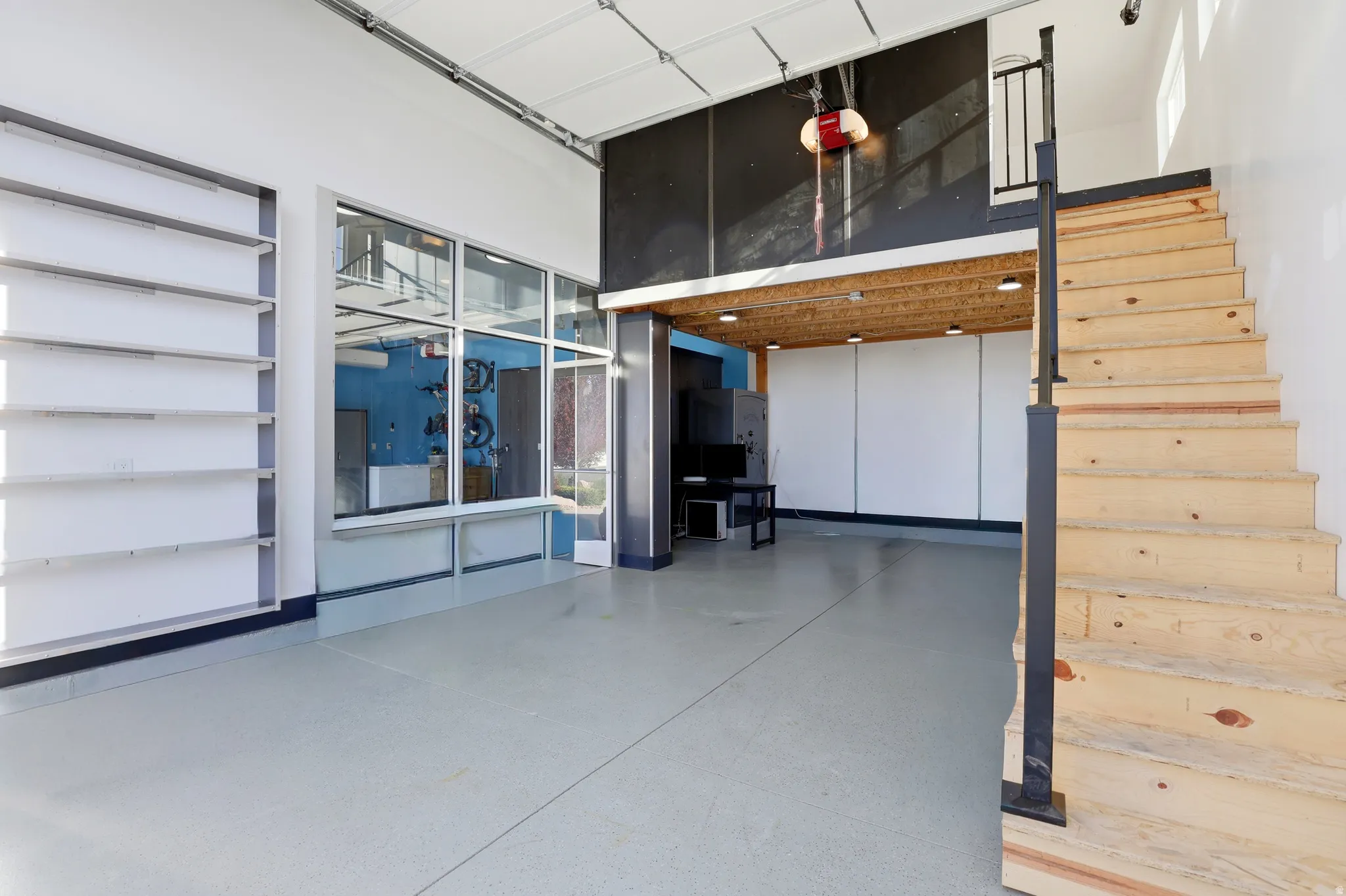 Spacious interior featuring a light gray epoxy floor and a prominent wooden staircase with a black metal handrail